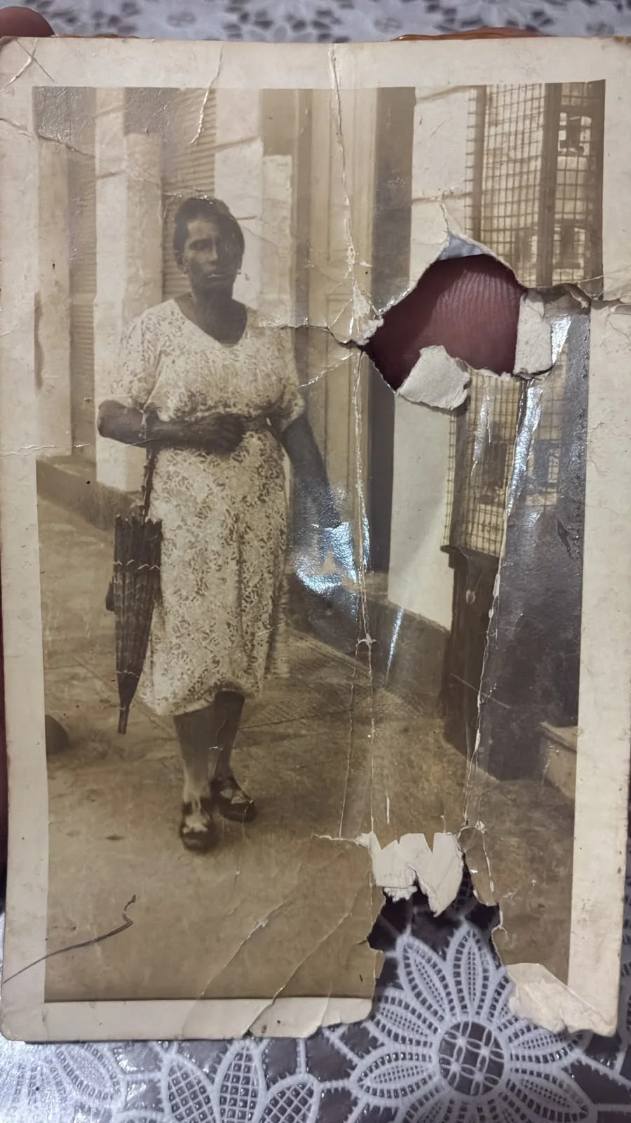 Foto antiga rasgada de uma mulher segurando uma sombrinha